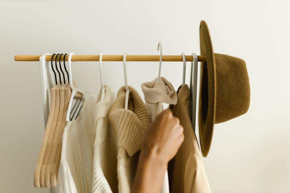 Stylish beige and brown clothes on a rack with a hand reaching in